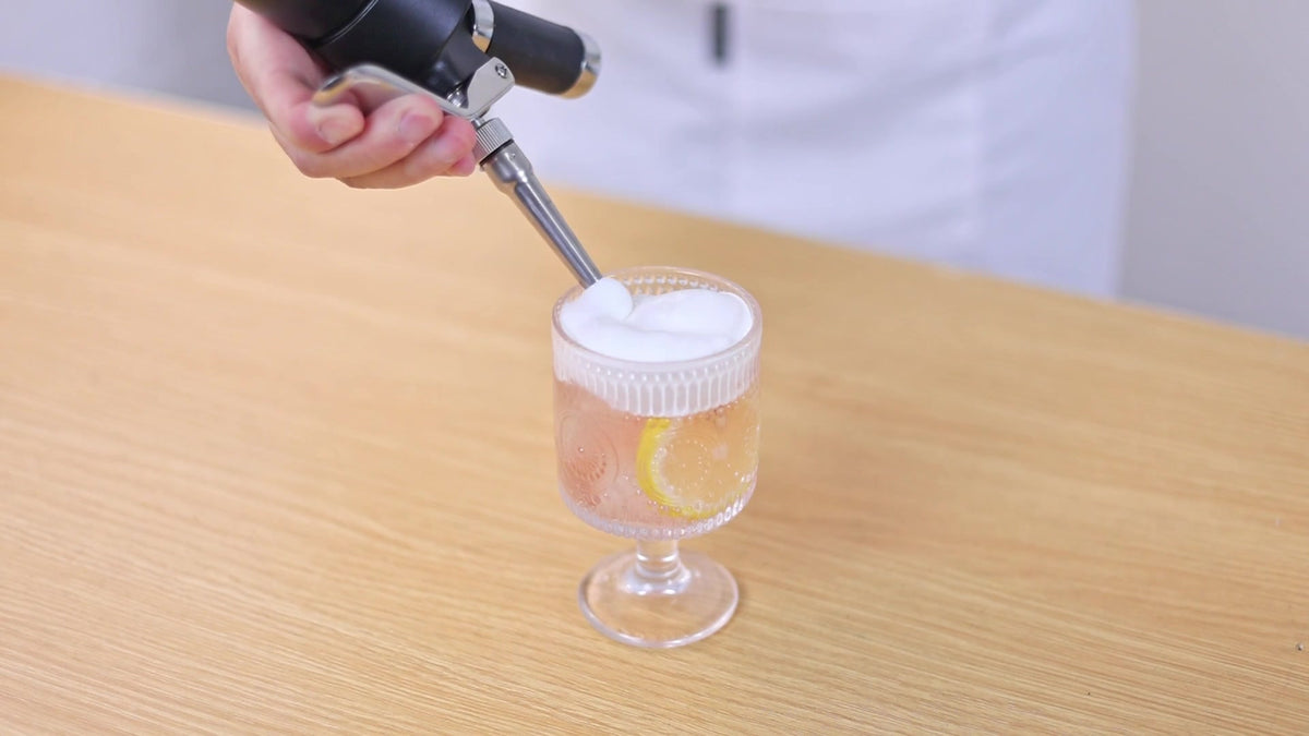 Cream whipper dispensing topping onto a drink, frame from original product demonstration video at 44 seconds